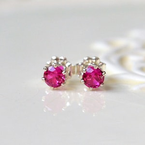 May include: A pair of silver stud earrings with a bright pink round gemstone in each earring.