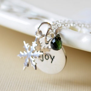 May include: Silver necklace with a snowflake charm, a green gemstone, and a round pendant with the word "JOY" engraved on it.