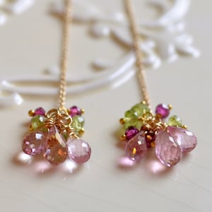 May include: A pair of gold earrings with pink and green gemstone drops. The earrings feature a cluster of small pink and green gemstones, and larger pink gemstone drops.