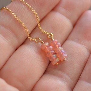 May include: A delicate gold chain necklace with a pendant made of pink opal stones. The pendant is made of two rows of stacked stones, each row with four stones.