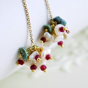 May include: Gold dangle earrings with a cluster of white pearls, red gemstones, and green stones.