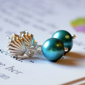 Könnte beinhalten: Ein Paar silberne Ohrringe in Tealblau mit Muschel-Design. Die Ohrringe haben eine tealblaue Perle.