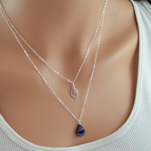 May include: A silver chain necklace with two pendants. One pendant is a silver feather and the other is a teardrop-shaped blue iridescent stone.