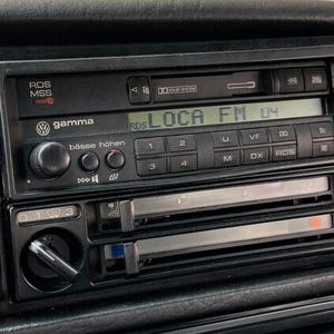 Puede incluir: Una radio de coche Volkswagen Gamma negra con una pantalla digital que muestra LOCA FM 04. La unidad cuenta con una ranura para reproductor de casetes, varios botones de control etiquetados como RDS, MSS y Dolby System, y rejillas de ventilación.