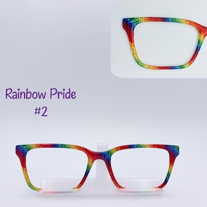 May include: Eyeglass frames featuring a vibrant rainbow-colored pattern across the entire rim. The frames have a rectangular shape with rounded corners. The text "Rainbow Pride #2" is printed in purple on the left side of the frame display.