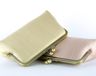 May include: Two satin clutch purses with gold metal frames. The top purse is a light beige color and the bottom purse is a light pink color.