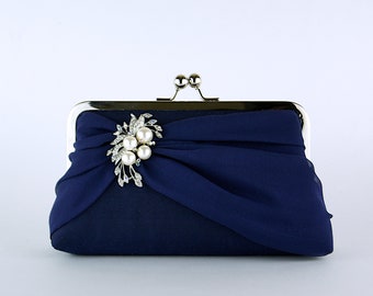 May include: A navy blue clutch purse with a silver clasp and a pearl and rhinestone embellishment.