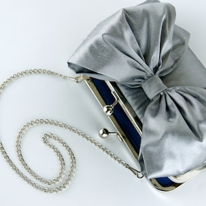 May include: A silver satin clutch bag with a large bow and a silver chain strap.