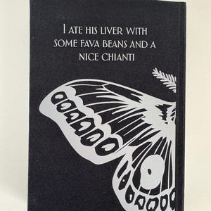 May include: A black book cover with the text "I ATE HIS LIVER WITH SOME FAVA BEANS AND A NICE CHIANTI" in white. A large, stylized butterfly wing design in white is featured on the lower portion of the cover.