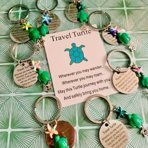 May include: A collection of travel-themed keychains featuring green turtle charms and engraved metal tags. The tags read "Travel Turtle" and include a travel-themed message. Some keychains have starfish and other charms.
