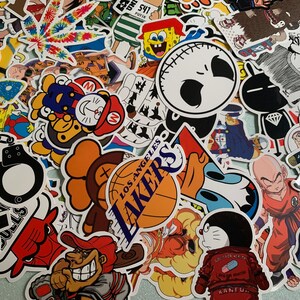 May include: A collection of colorful stickers featuring various designs. Includes cartoon characters like Spongebob, Doraemon, and characters from Dragon Ball Z. Also features a Los Angeles Lakers basketball, a marijuana leaf, and other graphics.