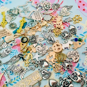 May include: A collection of assorted metal charms in silver, gold, and bronze tones. The charms include hearts, keys, stars, wings, and other decorative shapes. Some charms have text, such as "Faith can move mountains" and "LOVE".