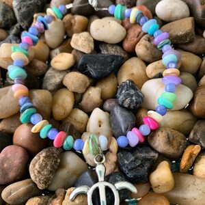 May include: A colorful beaded necklace with a silver turtle pendant. The necklace features a variety of pastel-colored beads, including pink, blue, green, and yellow. The turtle pendant is detailed and adds a nautical touch.