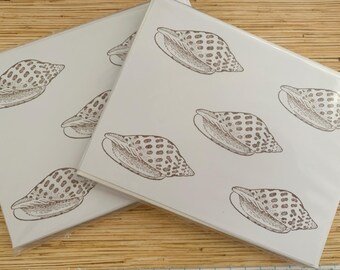 May include: Two stacks of white paper with a repeating pattern of brown seashell illustrations. The seashells are detailed with dotted patterns and curved lines, creating a natural, coastal theme.