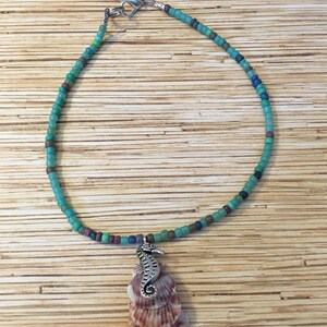 May include: A beaded necklace with a seahorse pendant and a seashell charm. The necklace features turquoise, blue, and brown beads. The pendant is silver-colored, and the seashell charm is white and brown.