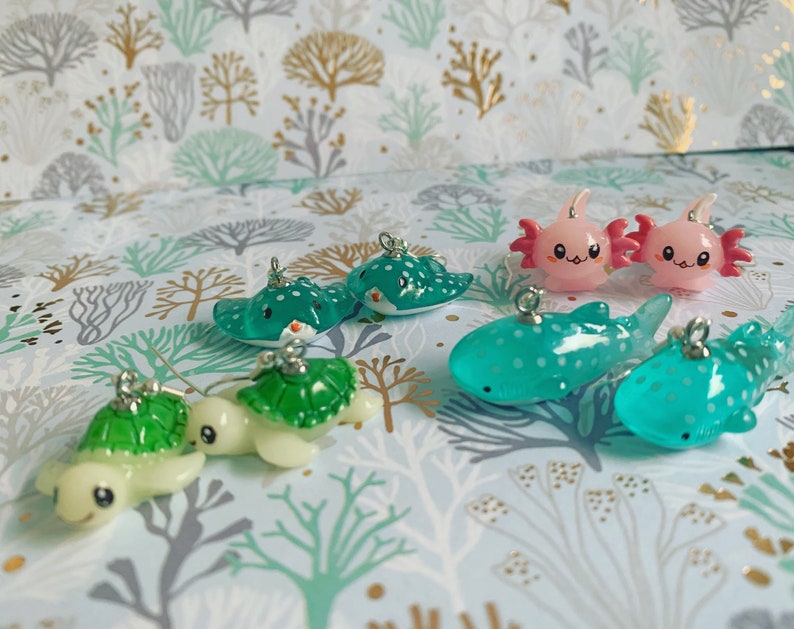 May include: A collection of miniature ocean-themed charms. The charms include sea turtles, stingrays, axolotls, and whale sharks in various shades of green, pink, and white. Each charm has a silver loop for attaching to jewelry or other crafts.