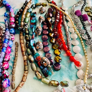 May include: A collection of colorful beaded necklaces in various styles. The beads are made of glass, stone, and other materials, in shades of red, blue, purple, and green. Some necklaces have intricate designs.