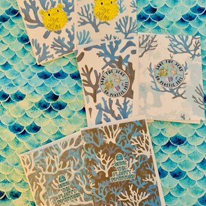 May include: A collection of greeting cards with ocean-themed designs. The cards feature illustrations of coral, pufferfish, and sea creatures. Text includes "Save Ocean," "Save the Seas, Go Plastic Free," and "Save the Floaty Potatoes." The background is a blue scale pattern.