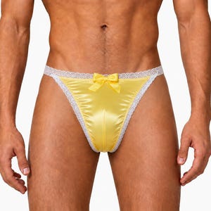 May include: A bright yellow satin thong featuring a delicate white lace trim along the edges and a small matching yellow satin bow centered at the waistband. The garment has a smooth, shiny finish and a classic high-cut design.