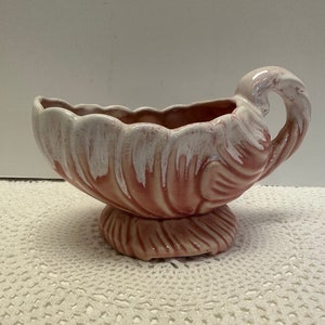 May include: A pink and white ceramic planter with a scalloped edge and a handle. The planter has a swirl design and a base.