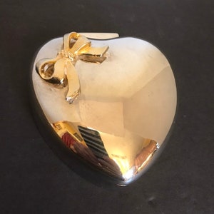 May include: A silver heart-shaped trinket box with a gold bow on the top.