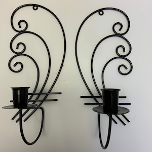 May include: A pair of black metal wall sconces with a decorative scroll design and candle holders.