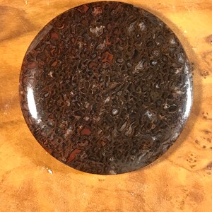 Puede incluir: Una piedra redonda y pulida con un patrón de mármol marrón y negro. La piedra tiene un acabado liso y brillante.