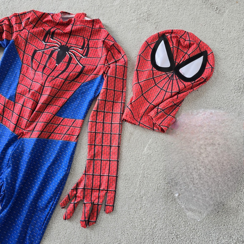 Puede incluir: Un disfraz de Spider-Man rojo y azul con una m&aacute;scara a juego. El disfraz presenta un emblema de ara&ntilde;a negra y un patr&oacute;n de telara&ntilde;a. La m&aacute;scara tiene forma de ojos blancos.