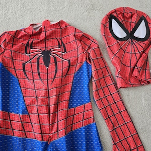 Puede incluir: Un disfraz de Spider-Man rojo y azul con una m&aacute;scara a juego. El disfraz presenta un emblema de ara&ntilde;a negro en el pecho y un patr&oacute;n de telara&ntilde;a. La m&aacute;scara tiene cubiertas para los ojos blancas y un patr&oacute;n de telara&ntilde;a.