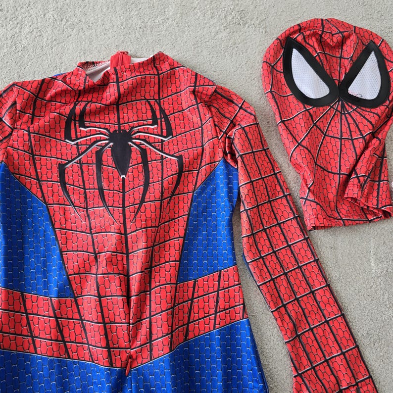 Puede incluir: Un disfraz de Spider-Man rojo y azul con una m&aacute;scara a juego. El disfraz presenta un emblema de ara&ntilde;a negro en el pecho y un patr&oacute;n de telara&ntilde;a. La m&aacute;scara tiene cubiertas para los ojos blancas y un patr&oacute;n de telara&ntilde;a.