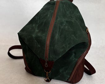 Peut inclure: Un sac à dos vert foncé avec des détails marron. Le sac présente un design angulaire unique, une fermeture éclair marron et une petite poignée. Le bas et les tirettes sont marron. Le sac a un style minimaliste.