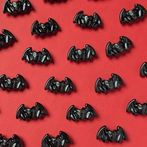 Può includere: Un motivo ripetuto di decorazioni nere lucide a forma di pipistrello su uno sfondo rosso brillante. I pipistrelli sono distribuiti uniformemente, creando un design ripetitivo. L'immagine è una vista dall'alto, ideale per Halloween o lavori a tema.
