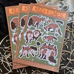 Puede incluir: Tres hojas de pegatinas con ilustraciones de zorros rojos en varias poses. Las pegatinas tienen un borde marrón y las palabras "RED FOXES" en la parte superior. El fondo es verde con ilustraciones de huesos.