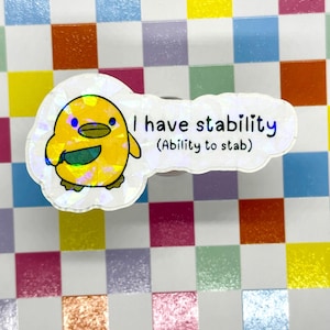 Pode incluir: Um autocolante holográfico com um pintinho amarelo de desenho animado com uma barriga verde. O autocolante tem o texto "I have stability (Ability to stab)" em azul e preto. O fundo é um padrão xadrez colorido.