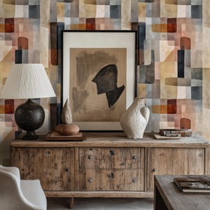 Puede incluir: Un aparador de madera rústica con una lámpara, obras de arte y jarrones decorativos. La obra de arte presenta una forma abstracta negra sobre un fondo beige. El papel pintado detrás del aparador tiene un patrón geométrico en tonos marrones, beige y grises.