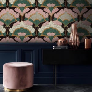 May include: Interior shot with a dark floral wallpaper in pink, green, and gold fan patterns. A pink velvet ottoman with a gold base is in front of a dark blue paneled wall. A black console table displays copper-toned decorative items.