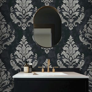 Könnte beinhalten: Badezimmer-Waschtisch mit schwarzem Schrank, weißer Arbeitsplatte und goldenen Armaturen. Der ovale Spiegel reflektiert die dunkle Wand mit silbernem Damastmuster. Ein Seifenspender und eine Lotion stehen auf der Theke.