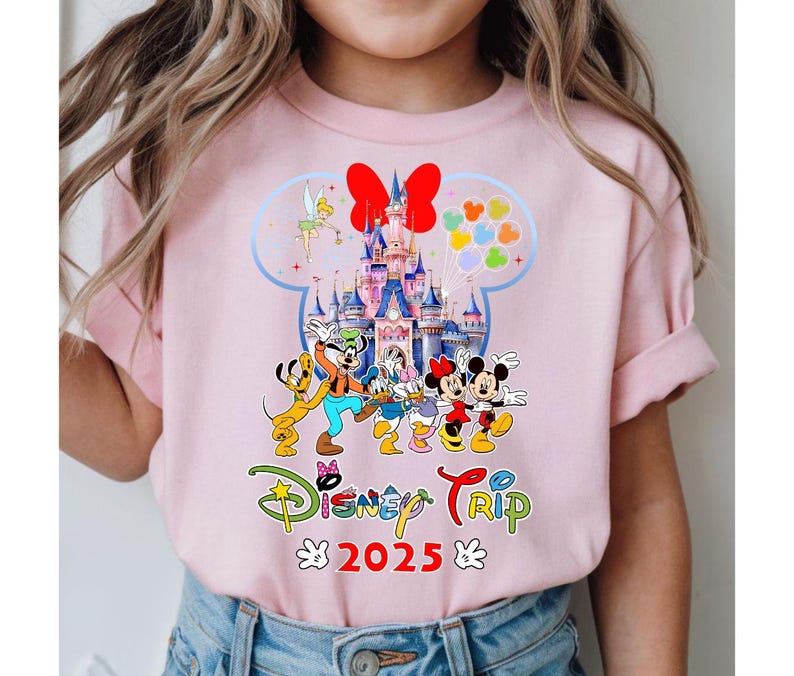 May include: Pale pink t-shirt with a vibrant Disney-themed graphic. The design includes Mickey and Minnie Mouse, a castle, and the text "Disney Trip 2025". The overall design is bright and cheerful.