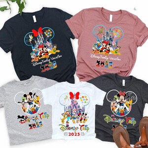 May include: Collection of short-sleeved t-shirts with Disney characters. Designs feature Mickey and Minnie Mouse, Donald Duck, and Goofy, with text reading "Disney Family Vacation 2023" and "Disney Trip 2023". Colours include black, pink, grey, and white.