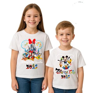May include: Two children wearing white t-shirts with Disney character designs. The shirts display Mickey Mouse, Minnie Mouse, Donald Duck, and Goofy, with the text "Disney Family Vacation 2025" and "Disney Trip 2025" in colourful lettering.