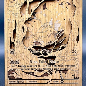 May include: Wooden Ninetales Pokémon card featuring a layered design. The card includes the text "Ninetales," "Will-O-Wisp," and "Nine-Tailed Dance." The card is supported by a small wooden stand.