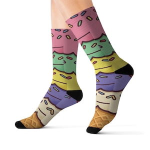 May include: Colorful socks featuring a stacked ice cream cone design. The socks display layers of pink, green, yellow, and purple ice cream with sprinkles, atop a waffle cone base. The heels and toes are black.