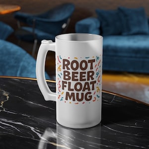 May include: A frosted glass mug with a white handle. The mug features the words "ROOT BEER FLOAT MUG" in brown letters, with colorful confetti accents. The mug is designed for beverages.