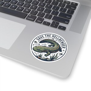Peut inclure: Un autocollant rond avec une illustration détaillée d'une salamandre hellbender dans un environnement aquatique. Le texte "SAVE THE HELLBENDER" est disposé en cercle autour de la salamandre. L'autocollant est sur un ordinateur portable.
