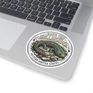 Peut inclure: Autocollant rond avec un dessin de salamandre hellbender verte et marron sur un lit de pierres. Le texte "SAVE THE HELLBENDER" est au-dessus de la salamandre, et "EASTERN UNITED STATES" en dessous.