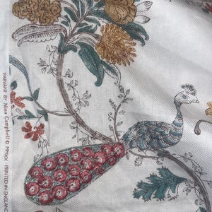 Peut inclure: Tissu crème avec un motif floral et paon détaillé. Le motif présente de grandes fleurs stylisées dans des tons or, marron et rouge, avec des feuilles et des branches turquoise. Un paon avec une queue en éventail est perché sur une branche.