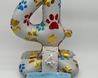 Könnte beinhalten: Silberner Ballon mit der Zahl 4 und Pfotenabdruck-Designs in Rot, Blau und Gold. Enthält eine passende Kerze und ein blaues Halstuch mit dem Text "Happy Birthday!".