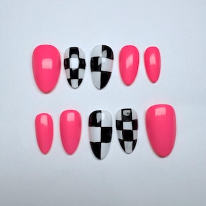 May include: Set of artificial nails in a variety of sizes. The nails are oval-shaped and feature a bright pink color and a black and white checkered pattern. The nails are arranged on a white surface.