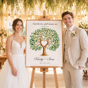 May include: A rectangular wedding guest book sign on a wooden easel featuring a watercolor tree with green fingerprint leaves and a heart-shaped trunk. The text reads: And the two shall become one, Genesis 2:24, Karly & Iam, May 12th, 2026.