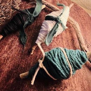 May include: Three decorative ornaments consisting of wooden twigs wrapped in yarn. One twig is wrapped in black yarn with a green ribbon, one in white yarn with a green ribbon, and one in teal yarn with a light-colored string tied in a knot.